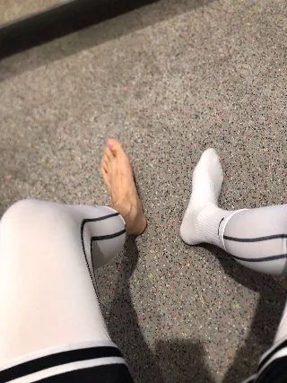 One bare foot, one socked foot, both in white tights with black stripes, teasing on speckled gym floor