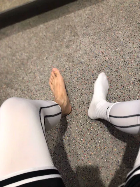 One bare foot, one socked foot, both in white tights with black stripes, teasing on speckled gym floor