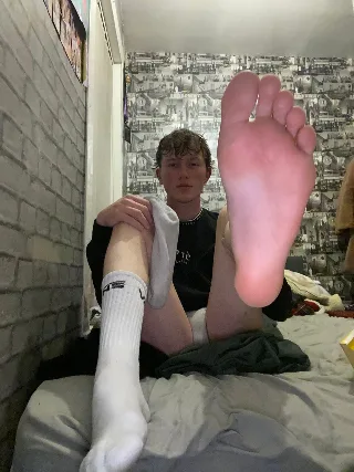 Freshly socked lad shows off his bare sole while lounging on bed with one foot up