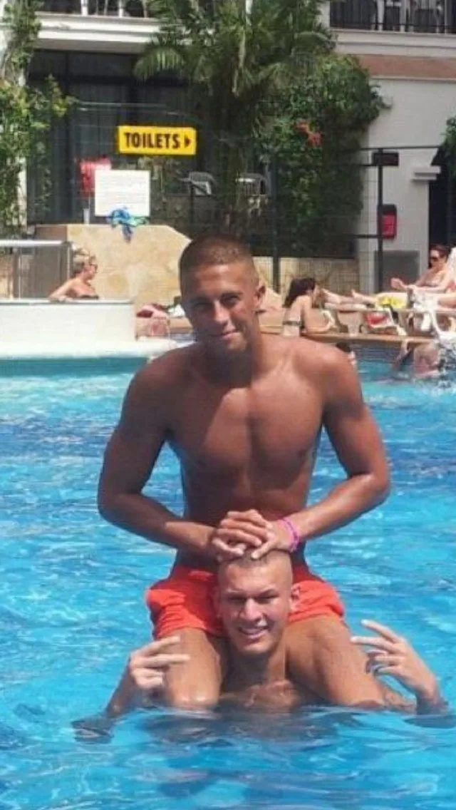 Dois caras gostosos brincam de cavalo na piscina, um montado nos ombros do outro, sem camisa e sorrindo