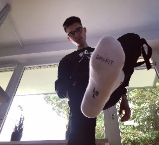 Geeky guy in glasses teases with socked foot thrust toward camera, Dri-Fit sole on display
