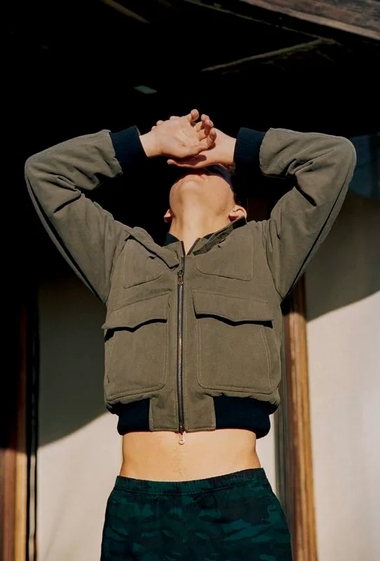 Tye Sheridan con giacca corta e addominali in mostra, mani dietro la testa, abbronzato e rilassato