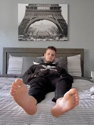 Lazy lad in Adidas tracksuit sprawls on bed, bare feet front and center for foot fetish fans