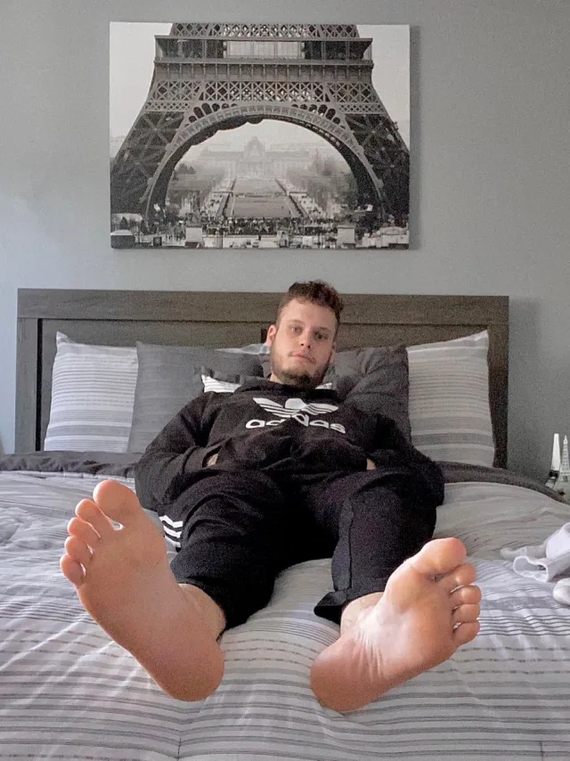 Lazy dreng i Adidas tracksuit sprøjter på sengen, bare fødder foran og center for fod fetich fans