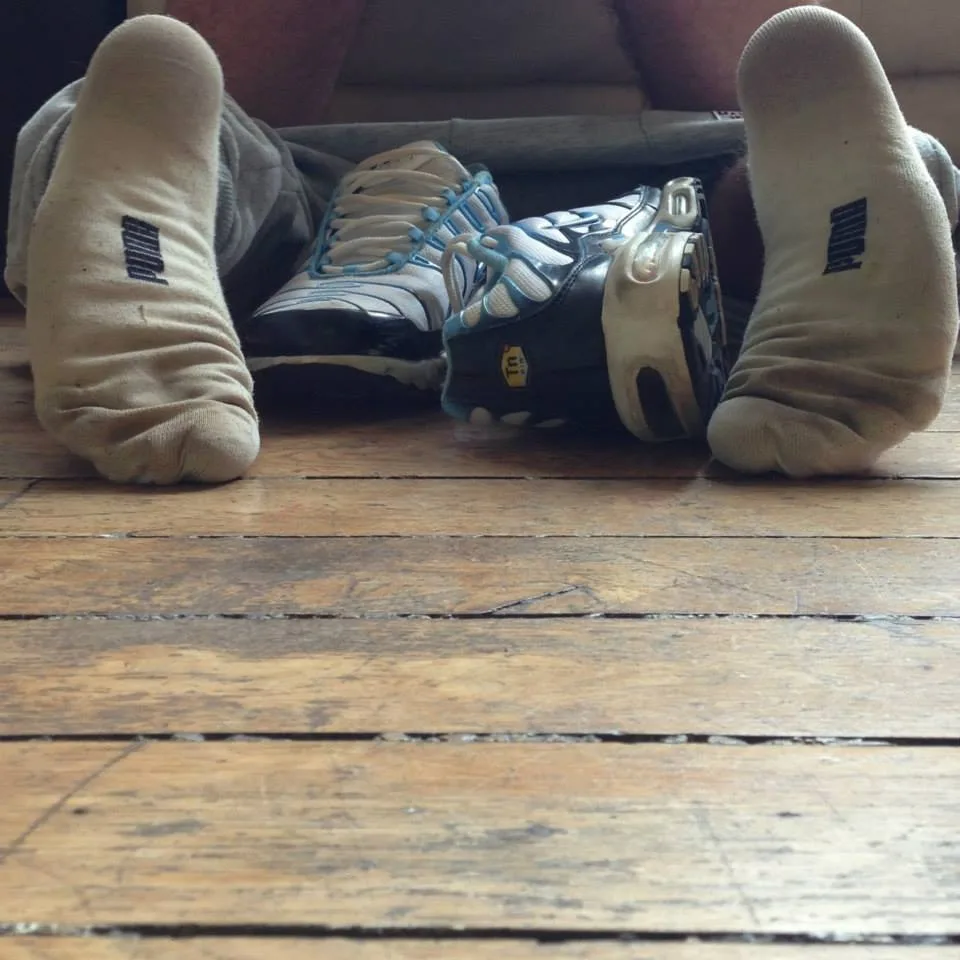 Dovne dreng i Puma sokker sparker tilbage med slidte sneakers ved siden af hans bare fødder på trægulv