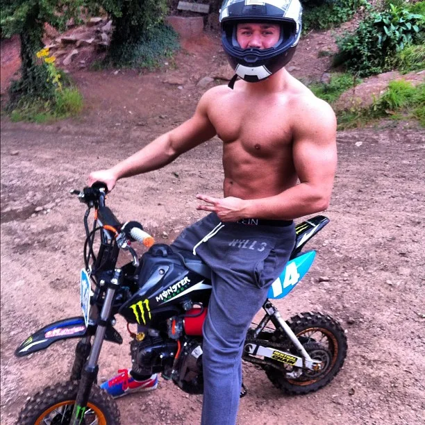 Skjult snavs cykel dreng i hjelm og trackies bøjning muskler ved siden af hans mini moto
