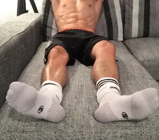 Muscular lad lounging on couch in socks, abs on display, feet front and center for foot fetish fans