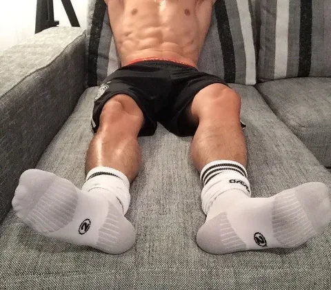 Muscular lad lounging on couch in socks, abs on display, feet front and center for foot fetish fans