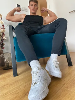 Muscular lad flexing biceps in tank top, white sneakers and socks on display