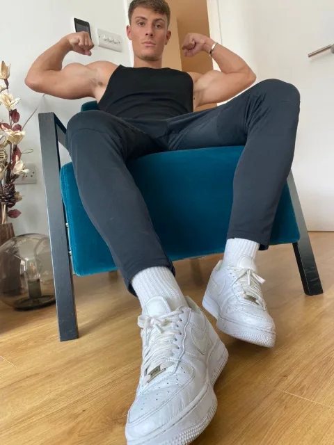 Muscular lad flexing biceps in tank top, white sneakers and socks on display