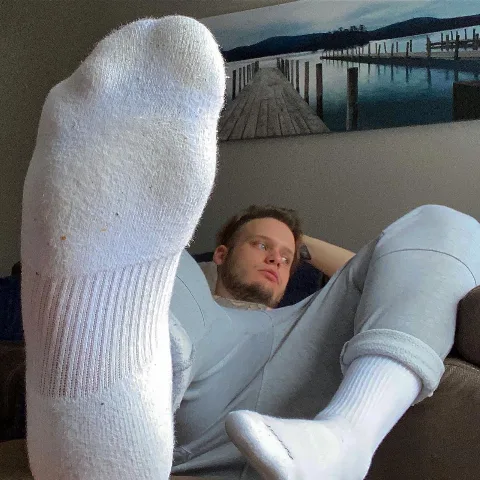 Lazy lad in white socks kicks back with feet up, grey sweats and a dreamy gaze