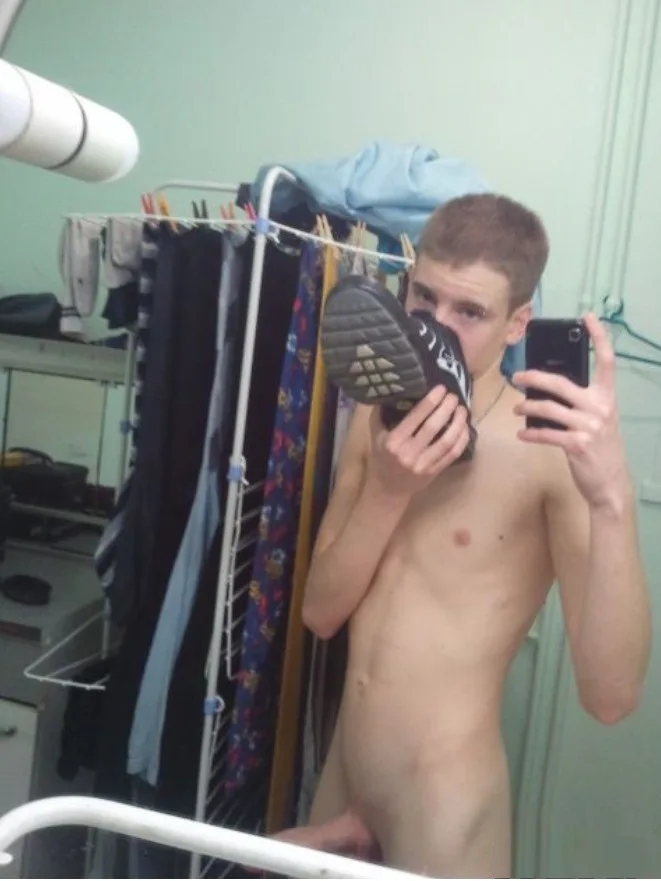 Unartiger Junge macht Spiegel-Selfie, Sneaker vors Gesicht haltend, nackte Brust und Beine zur Schau stellend