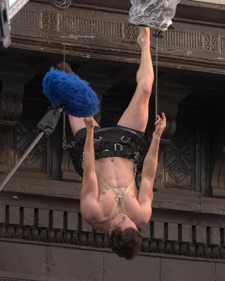 Tom Holland shirtless and upside down in harness, showcasing ripped abs and athletic physique on set