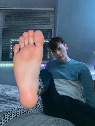 Lazy lad in jeans teases with bare sole, blue sweater framing his foot-fetish moment