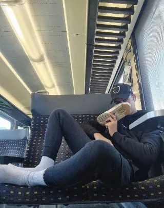 Lazy lad in hoodie and leggings lounging on train with socked feet up, shoe in hand