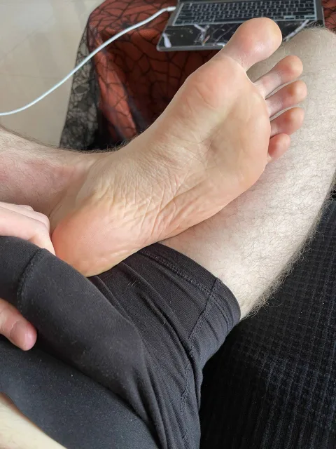 Lazy lad’s hairy legs and bare soles resting on his thigh, foot fetish focus