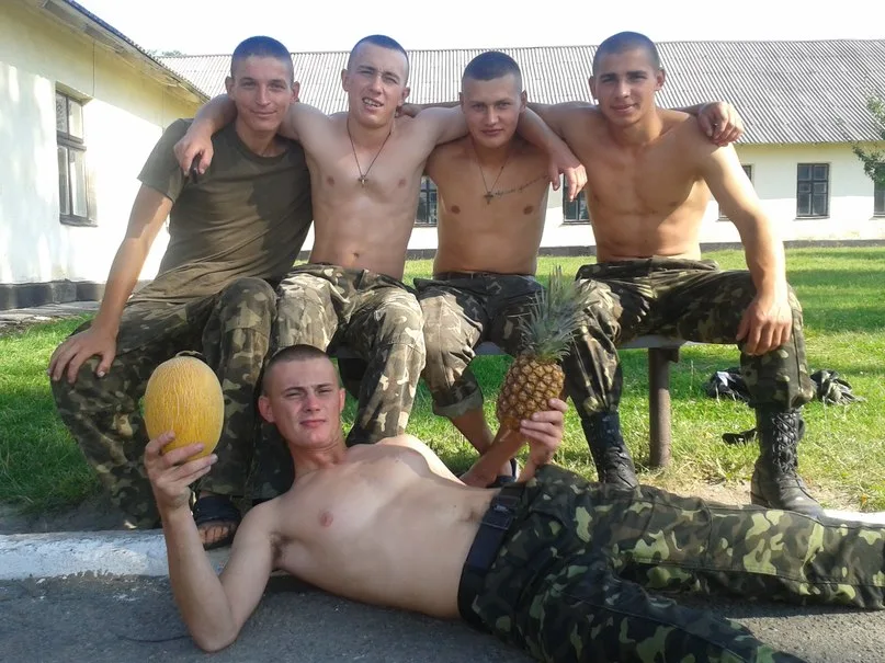 Fem skjoldløse military- stil fyre i camo bukser posere med frugt, en liggende bare- chested på fortovet
