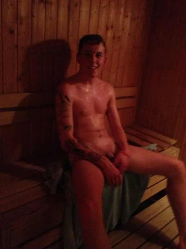 Garoto suado e quente na sauna, tatuado, posando nu no banco de madeira