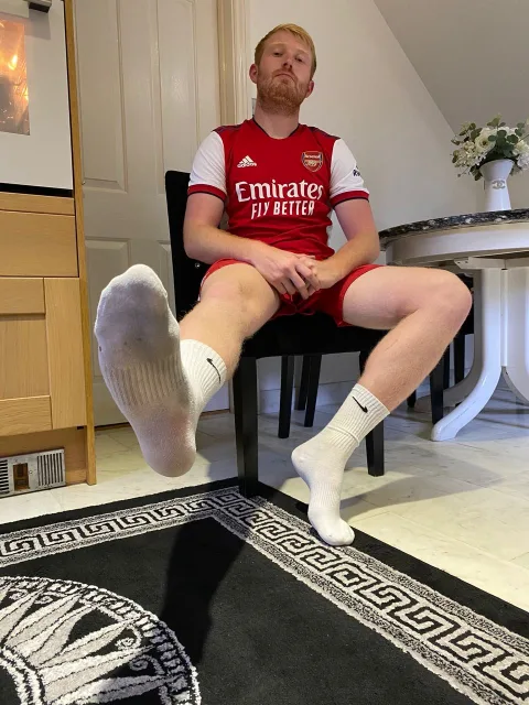 Foot-fetish guy in Arsenal kit flaunts socked soles while lounging shirtless on chair