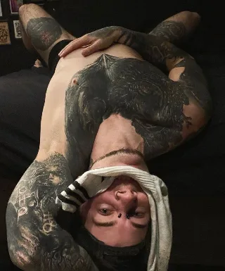 Tattooed guy lying back with feet up, showcasing soles and inked legs
