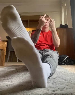 Lazy lad in socks flexes soles while flipping off the camera with a cheeky grin