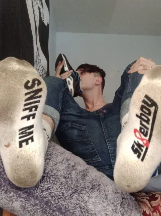 Guy in jeans sniffs sneaker while showcasing soles of dirty socks with bold text