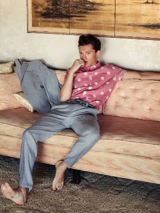 Tom Holland barefoot on plush couch, pink polka dots and grey slacks, feet front and center