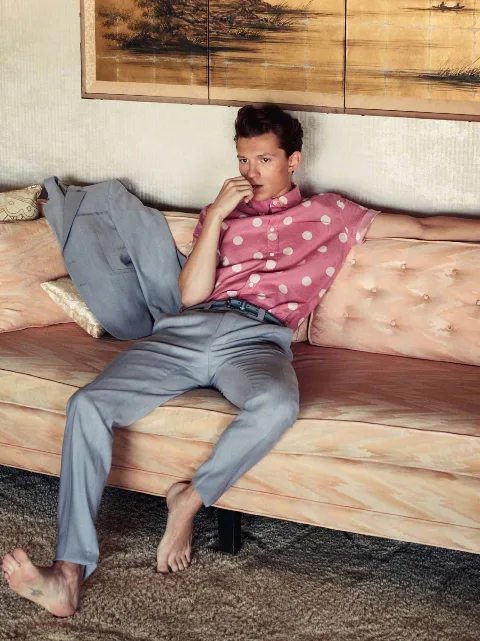 Tom Holland barefoot on plush couch, pink polka dots and grey slacks, feet front and center