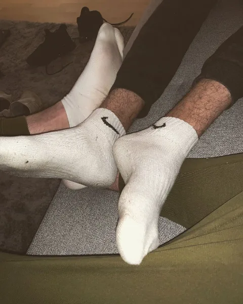 Lazy lad in white Nike socks with hairy legs sprawled on grey mat, feet front and center