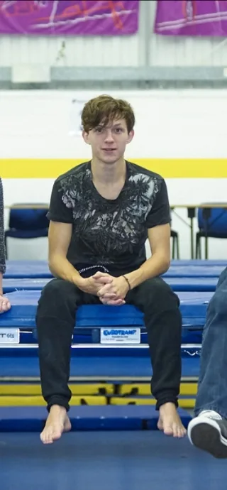 Tom Holland barefoot on gym bleachers, casual pose, feet front and center, no socks, no shoes