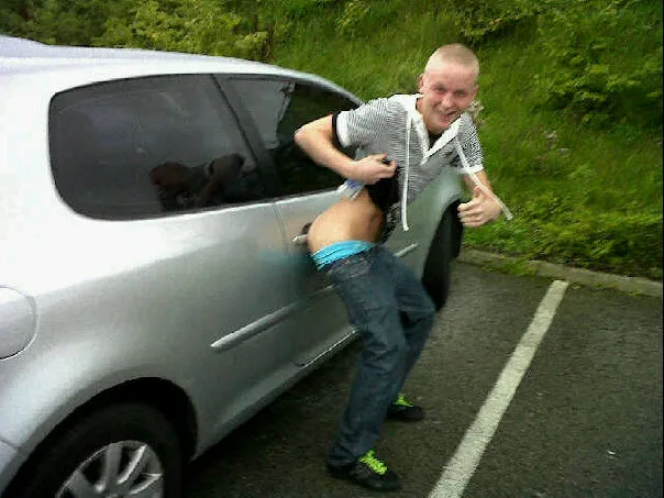 Cheeky lad flashing his bare ass in jeans by a silver car