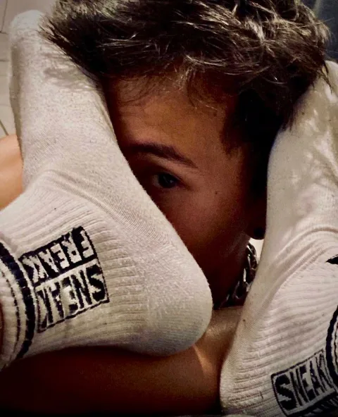 Sock-clad feet framing a peeking guy’s face, cheeky and intimate close-up