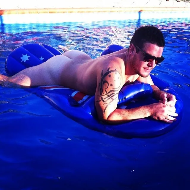 Sun- Kiss dreng lounging nøgen på Aussie float, tatoveret arm flexed, nuancer på, polstring vibes