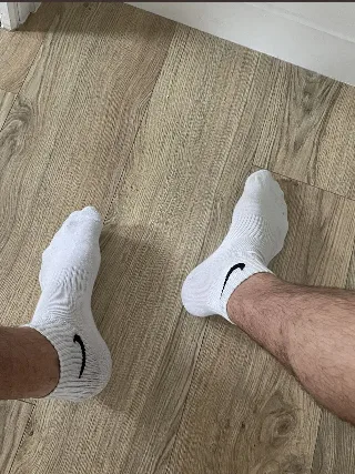 Hairy legs in white Nike socks spread wide on wood floor, foot fetish focus