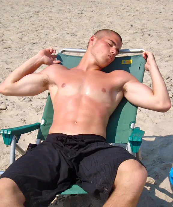 Sun- kysset strand dreng lounging shirtless i sorte svømmetunke, øjne lukket, afslappet på grøn stol