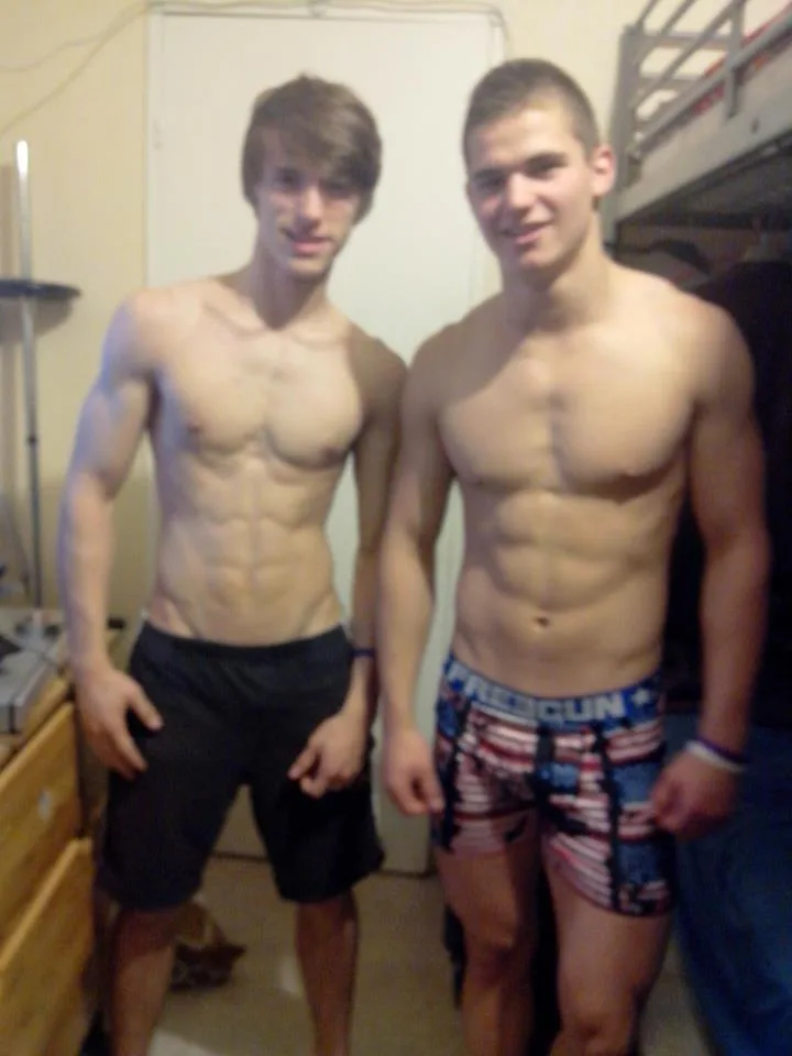 Two ripped lads posing shirtless in shorts, one in patriotic boxers, flexing abs for the camera