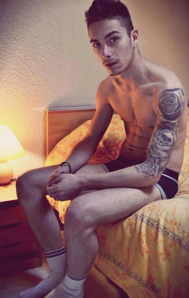 Hot tattooed lad in boxer briefs poses shirtless on bed with intense gaze