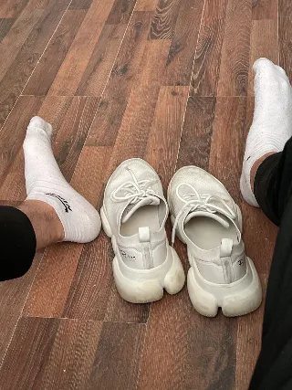 White socked feet stretched out beside chunky white sneakers on wood floor