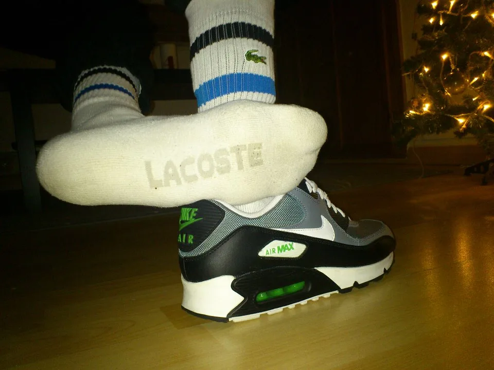 Facet w Lacoste skarpety teases podeszwa stopy nad Nike Air Max trampki, przytulny klimat wakacje