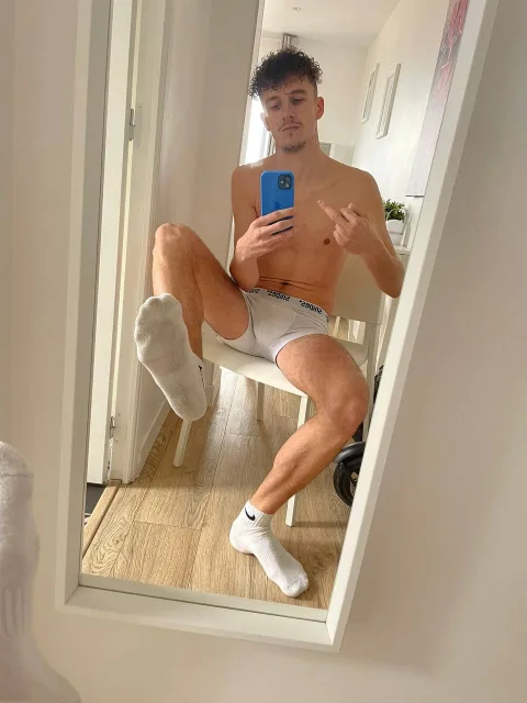 Curly-haired lad in white socks and boxers takes mirror selfie with one foot up, toes peeking out