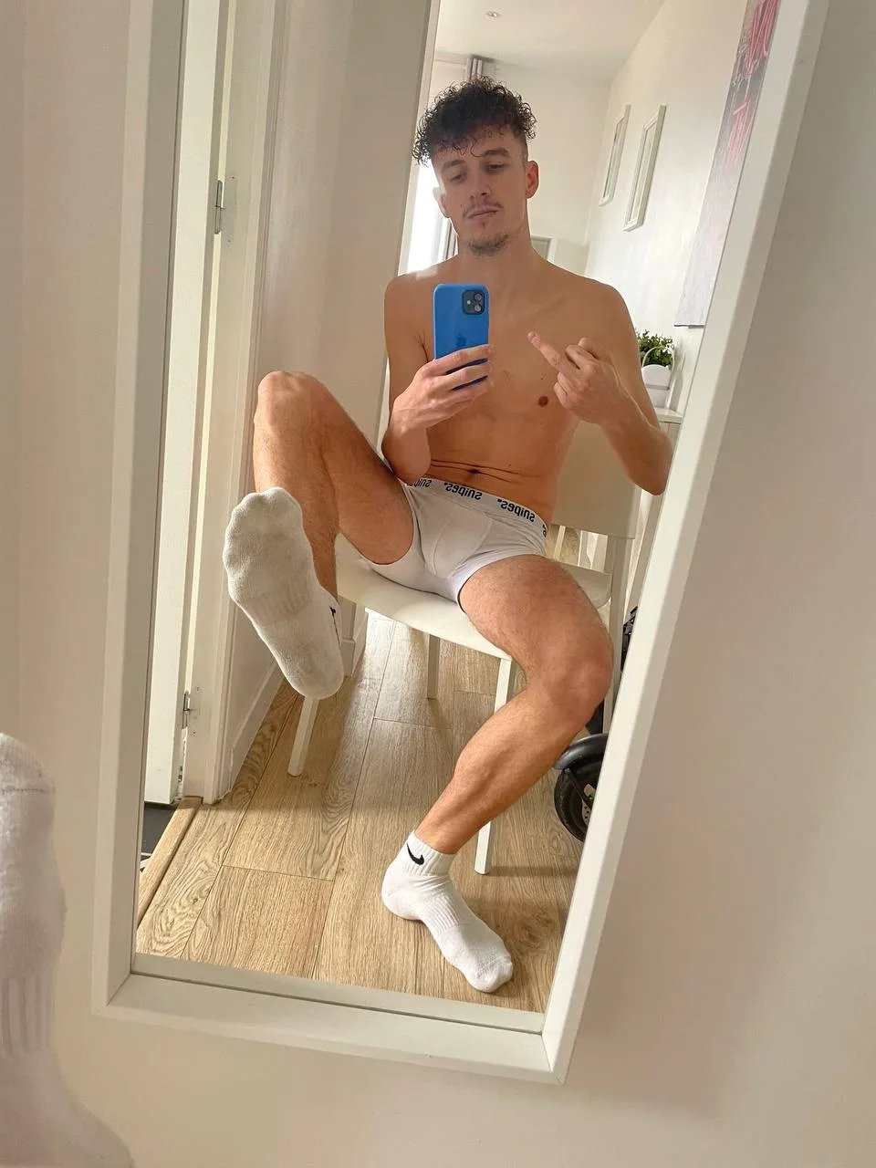 Krøllet dreng i hvide sokker og boksere tager spejl selfie med en fod op, tæer kigger ud