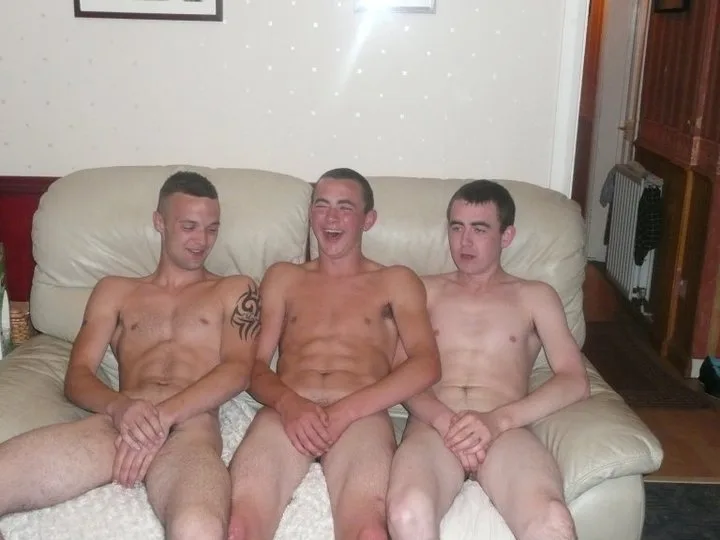 Three bare-chested lads laughing together on a couch, legs spread wide open