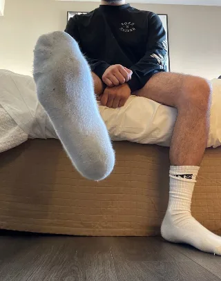 Guy in fuzzy socks flexes sole while lounging shirtless on bed, hairy legs on display