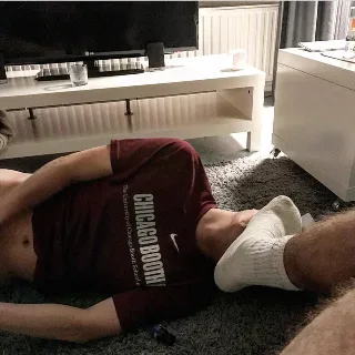 Lazy lad in maroon tee sprawled on rug, socked feet up, bare torso on display