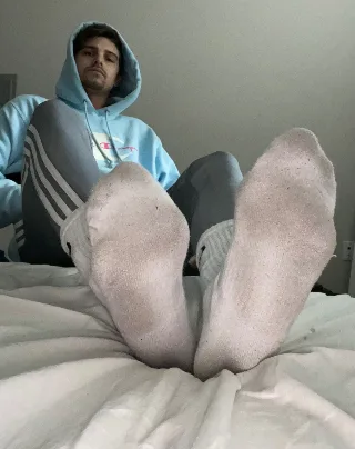 Lazy lad in hoodie shows off his socked soles while lounging on bed