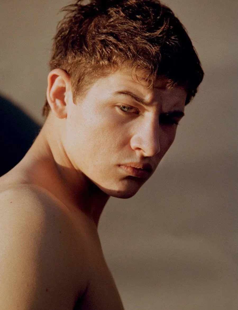 Hemdloser Tye Sheridan mit zerzaustem Haar und intensivem Blick, nackte Schultern im warmen Studio-Licht