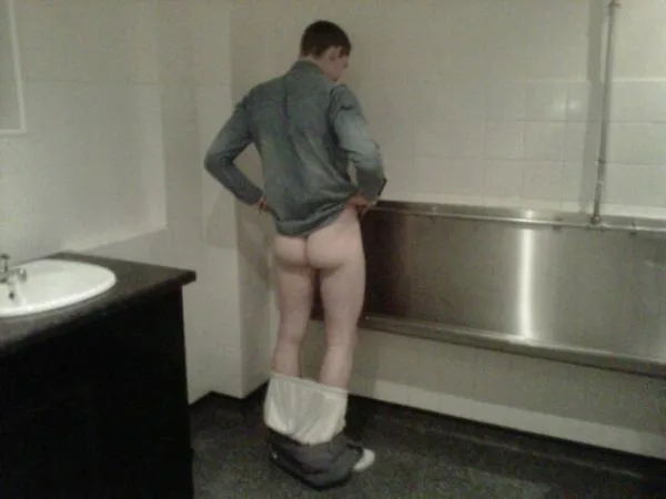 Guy caught mid-undress in bathroom, shirt down, pants around ankles, bare ass on display