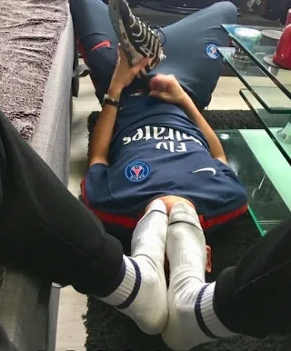 Guy in PSG jersey sprawled on floor, feet up, socks on, showing soles and toes while relaxing