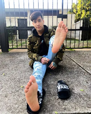 Foot-fetish guy in ripped jeans shows off bare soles and toes while lounging outdoors