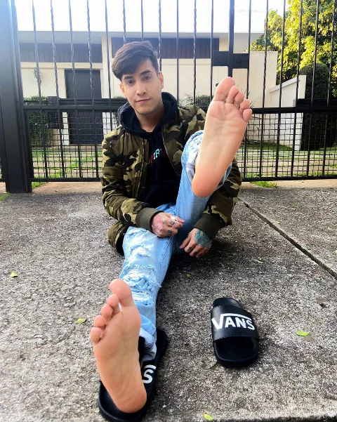Foot-fetish guy in ripped jeans shows off bare soles and toes while lounging outdoors